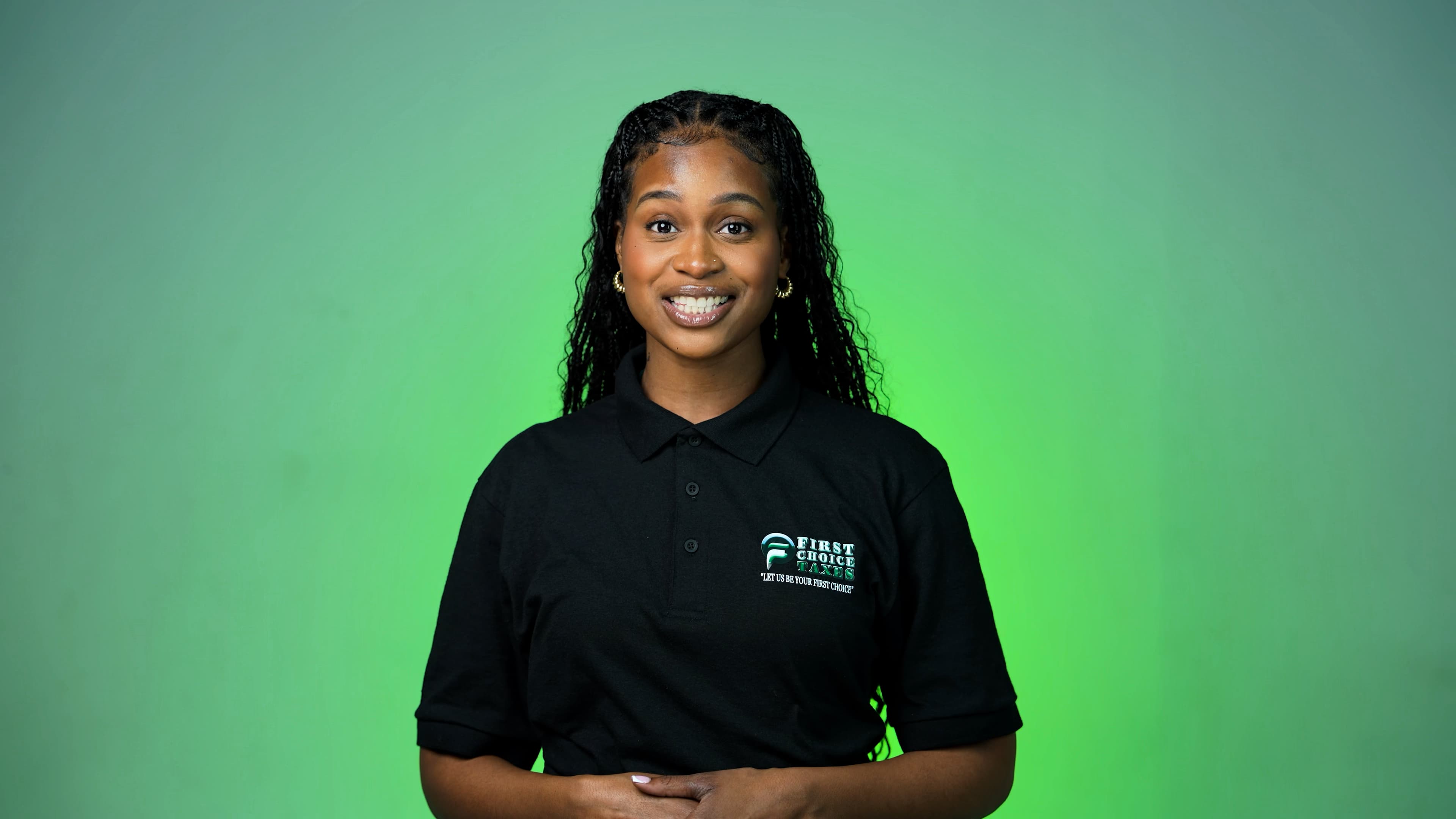 Smiling woman with long black braids in a black polo shirt against a green background.