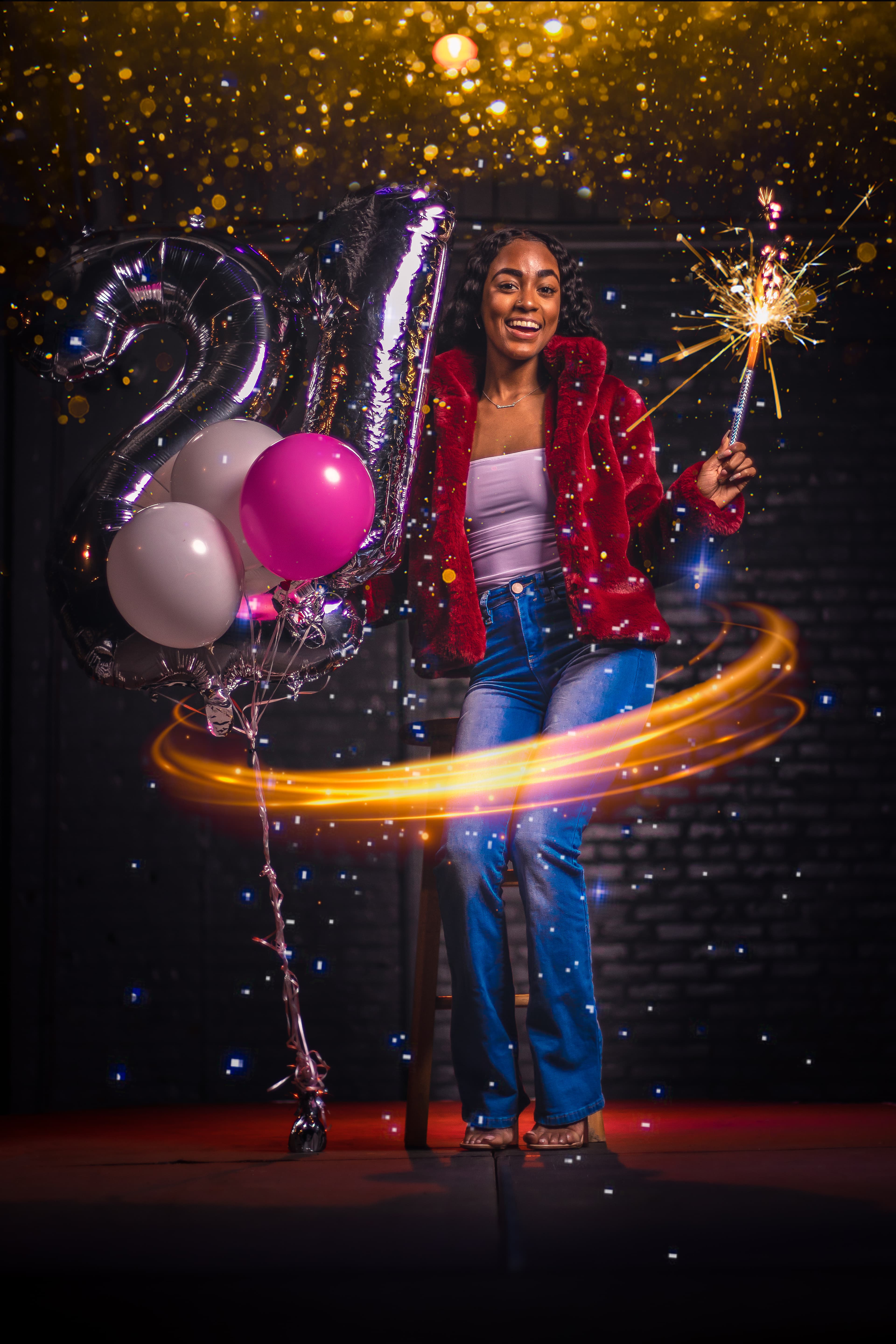 Smiling woman celebrates her 21st birthday with silver balloons, a sparkler, and festive golden glitter.