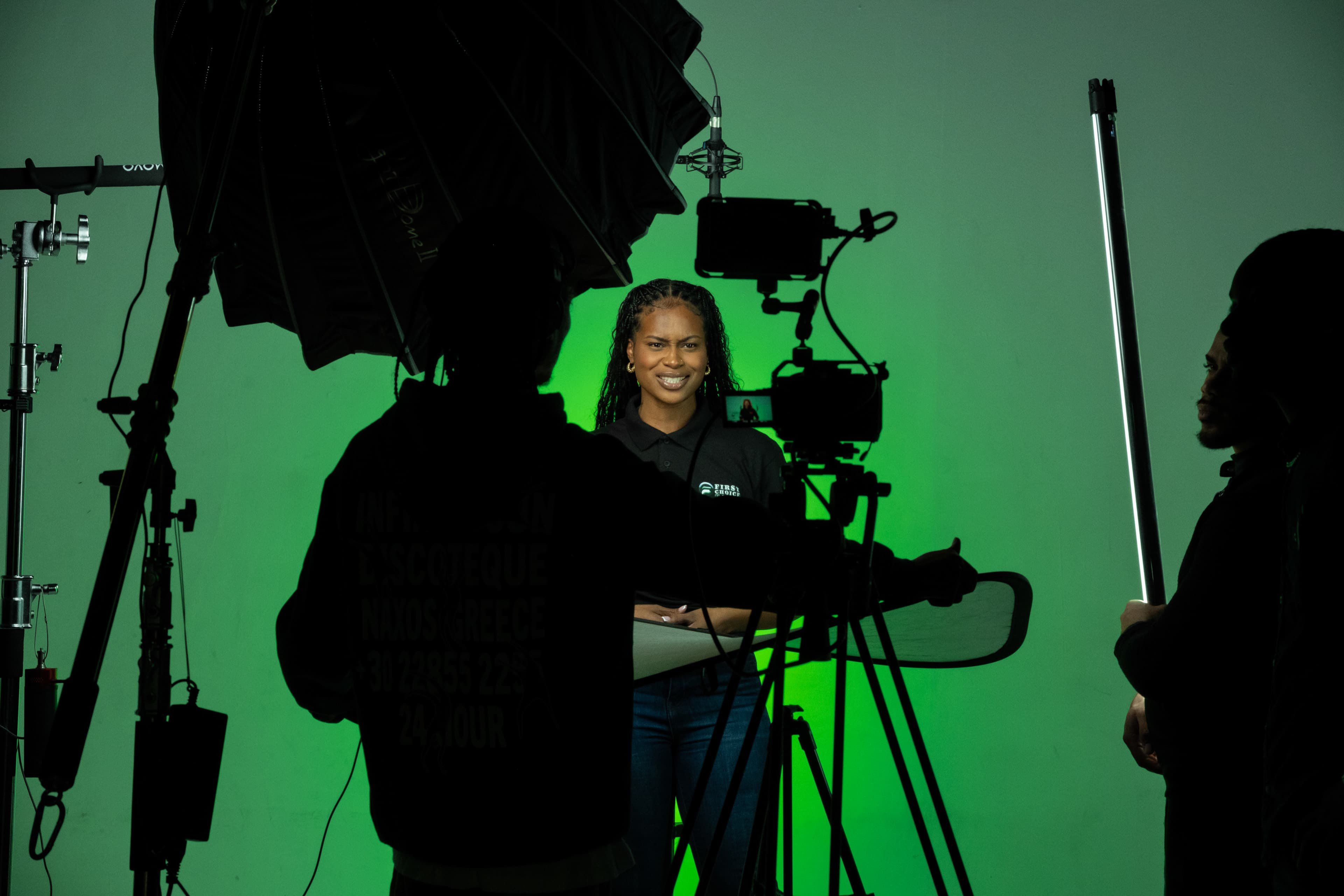 Woman smiling in front of green screen during professional video shoot with studio lighting equipment.