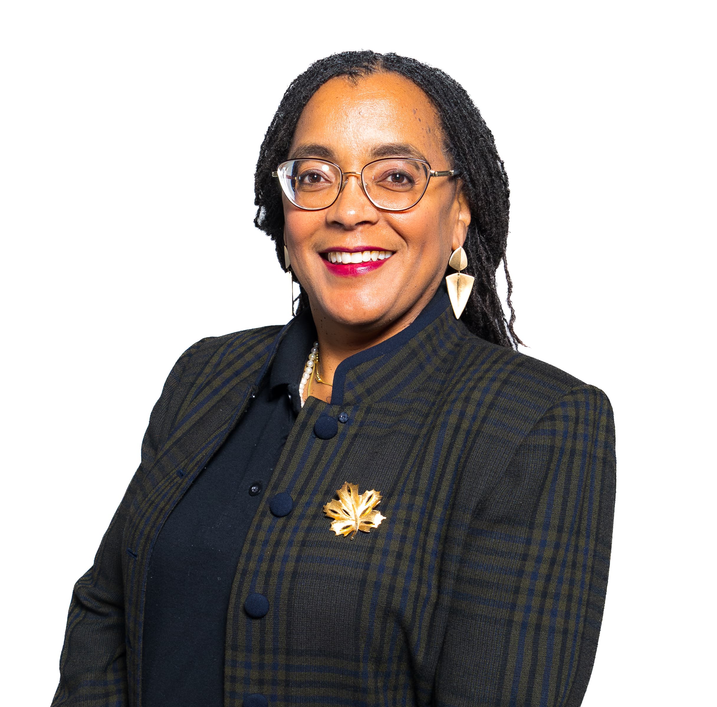 Smiling woman with braids and glasses wearing a plaid jacket and gold leaf brooch.