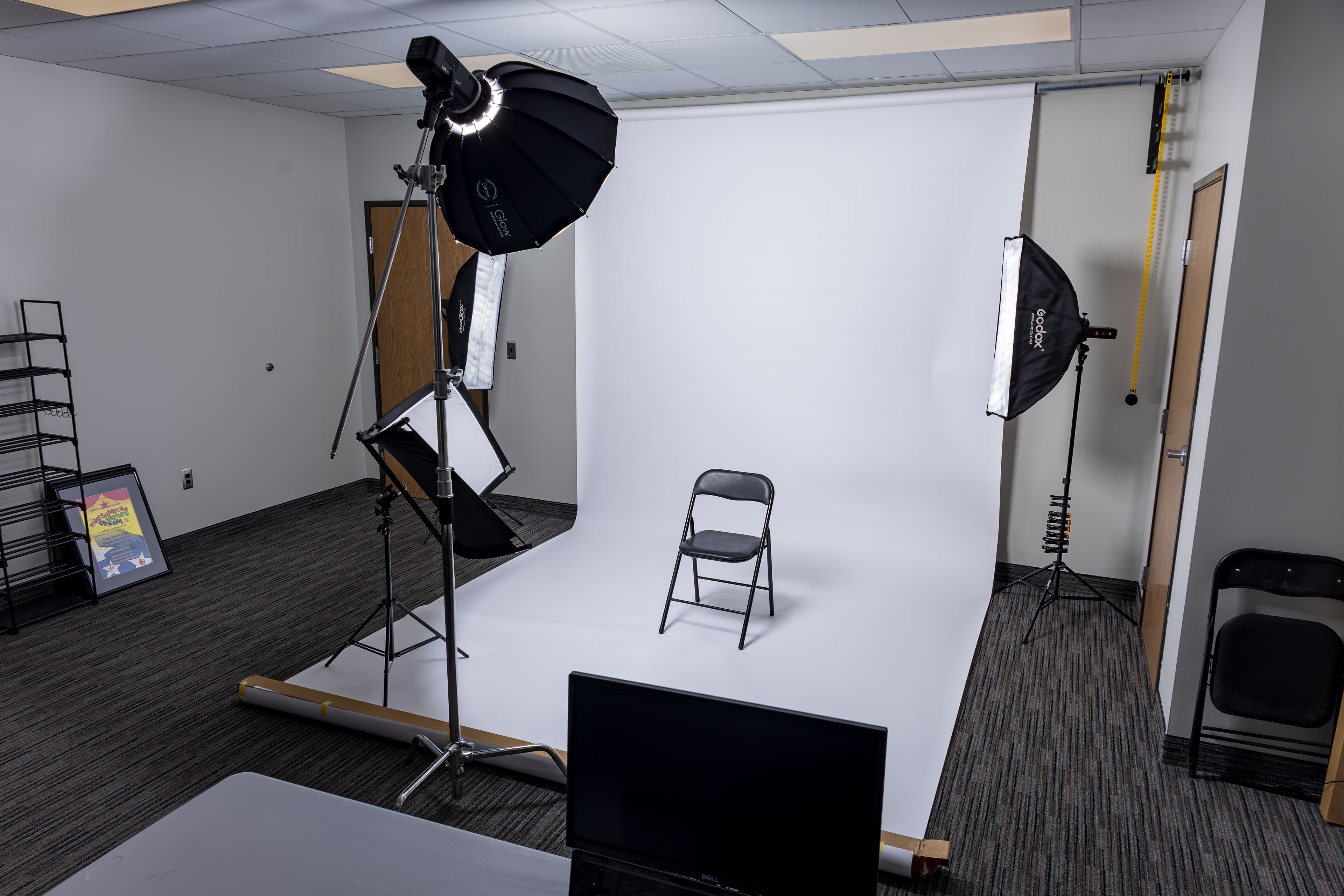 Professional photography studio setup featuring a white seamless backdrop, black chair, and studio lights.