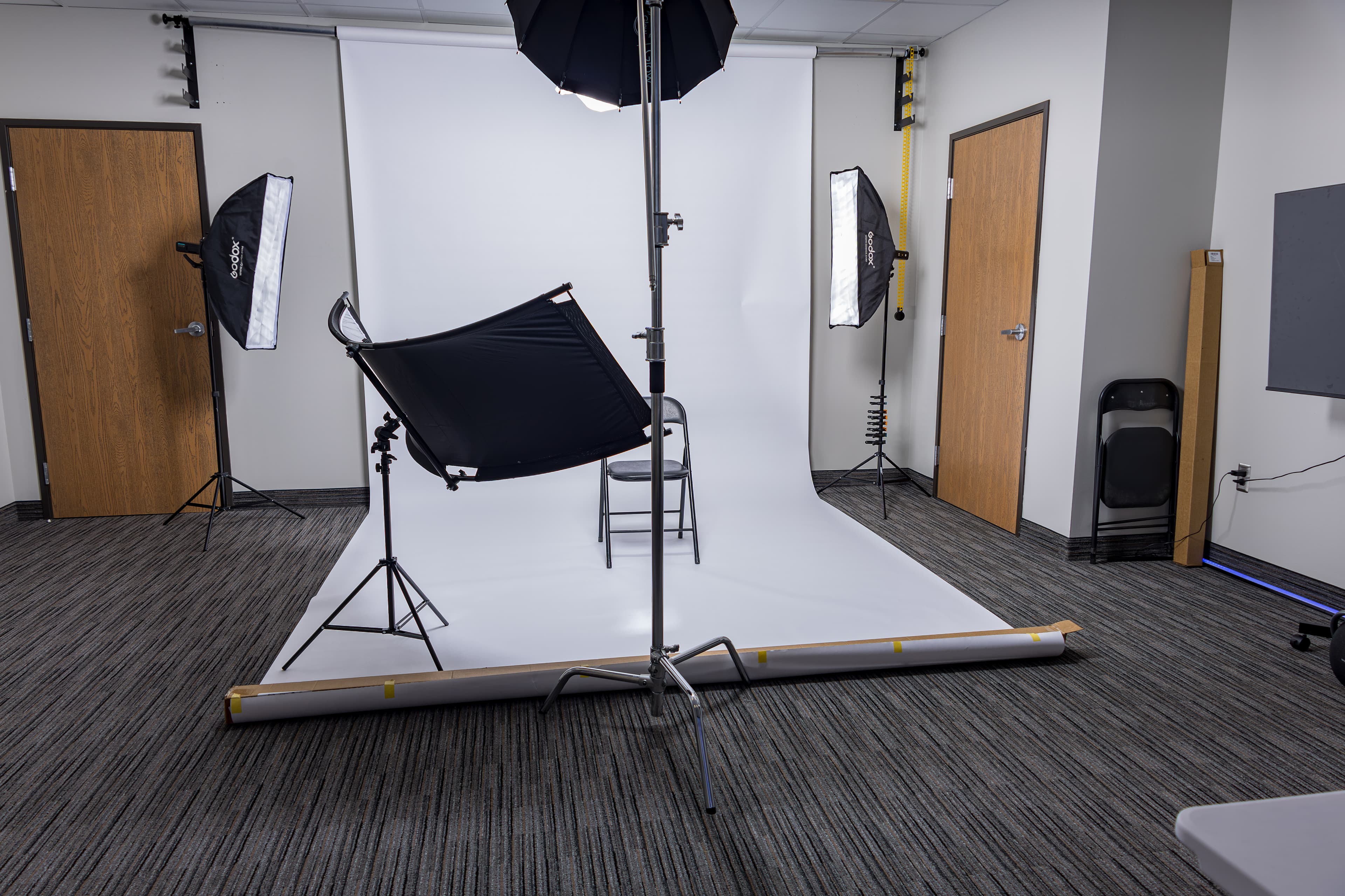 Professional photography studio setup with a white backdrop, studio lights, and a black chair.