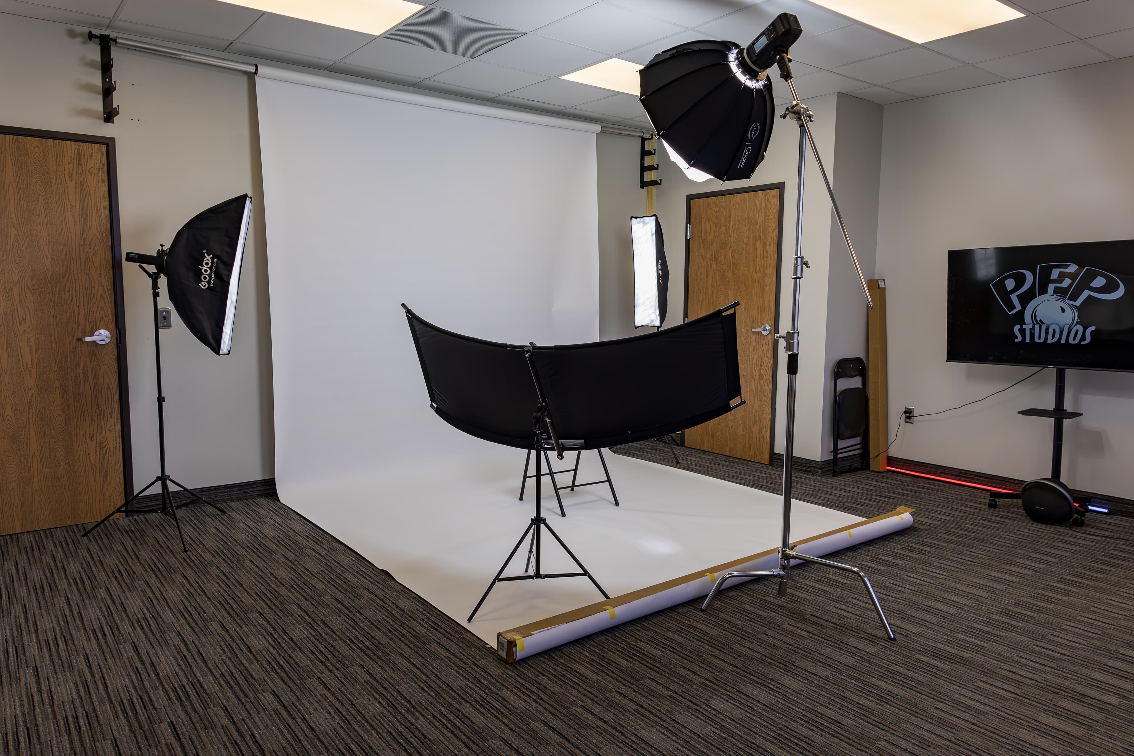 Professional photography studio featuring a white backdrop, softbox lighting, and a curved black reflector.