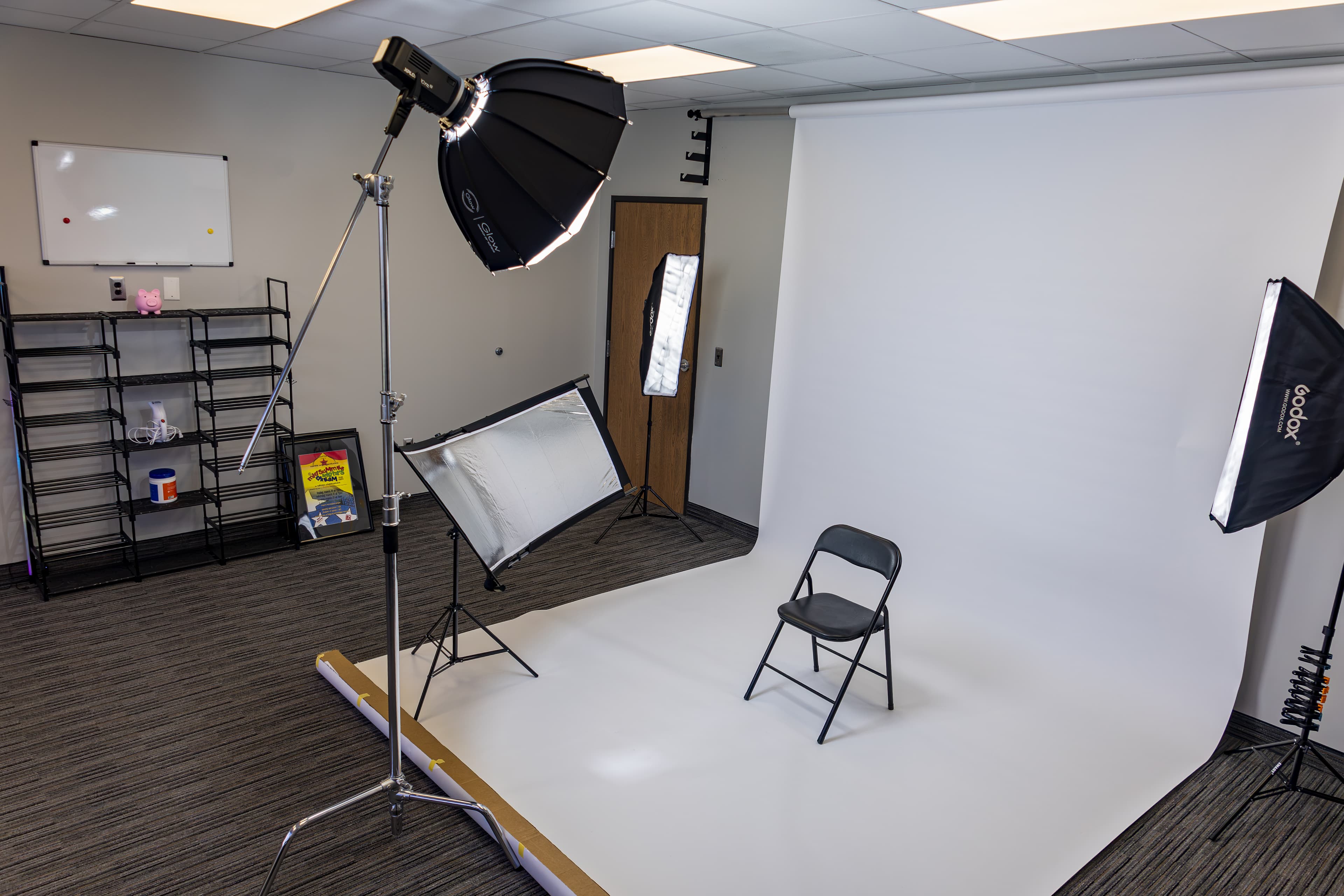 Photography studio featuring a white backdrop, a black folding chair, and professional lighting equipment.