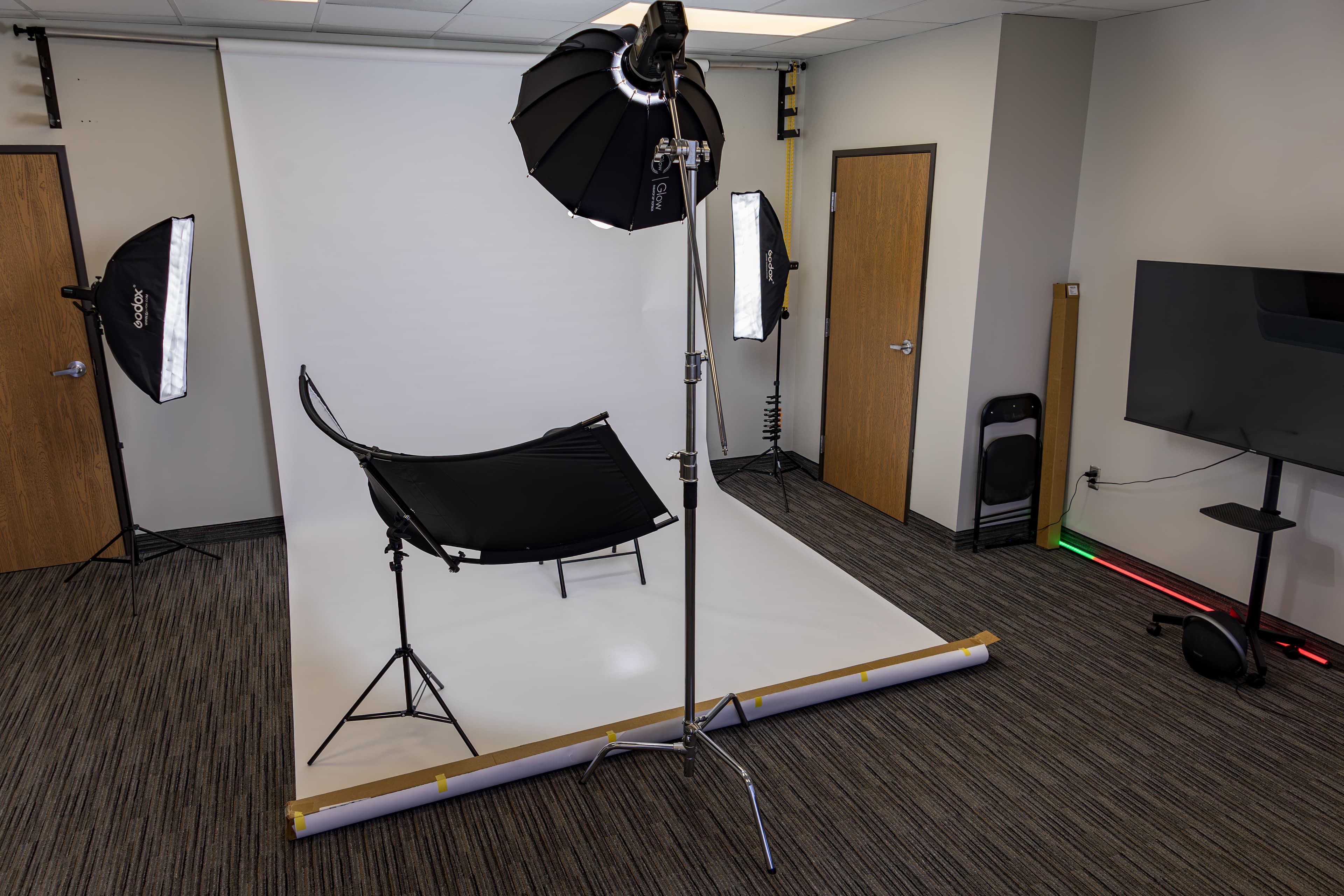 Professional photography studio setup with white seamless backdrop, softbox lights, and black curved reflector.