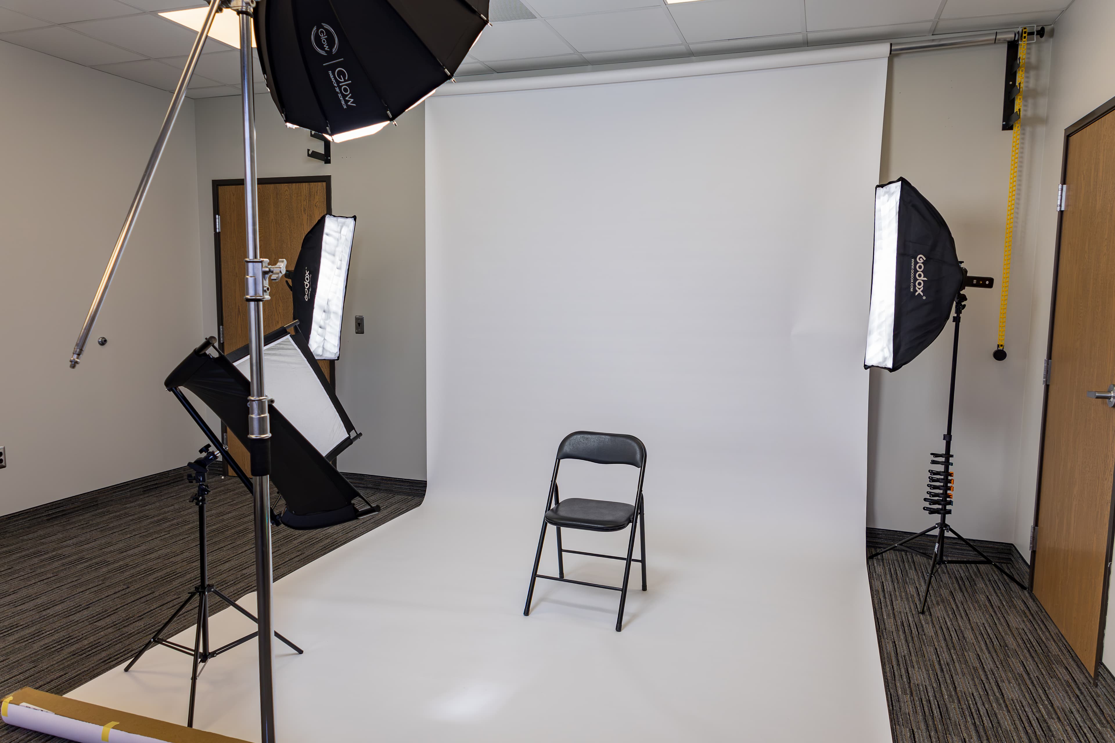 Professional photo studio with white backdrop, black chair, and multiple softbox lights on stands.