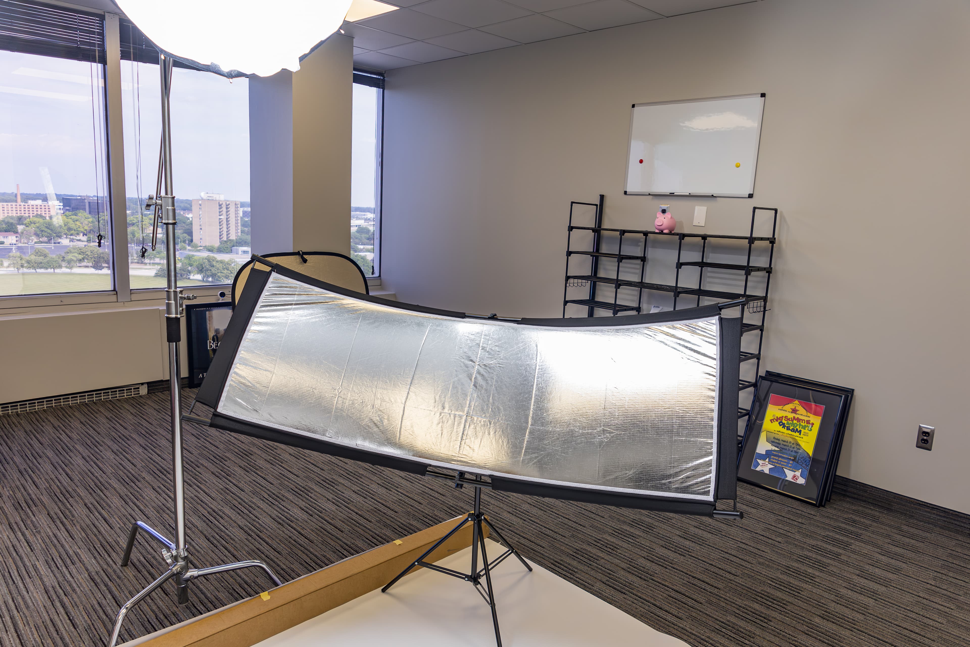 Curved silver reflector and studio light setup in an office overlooking a city skyline.