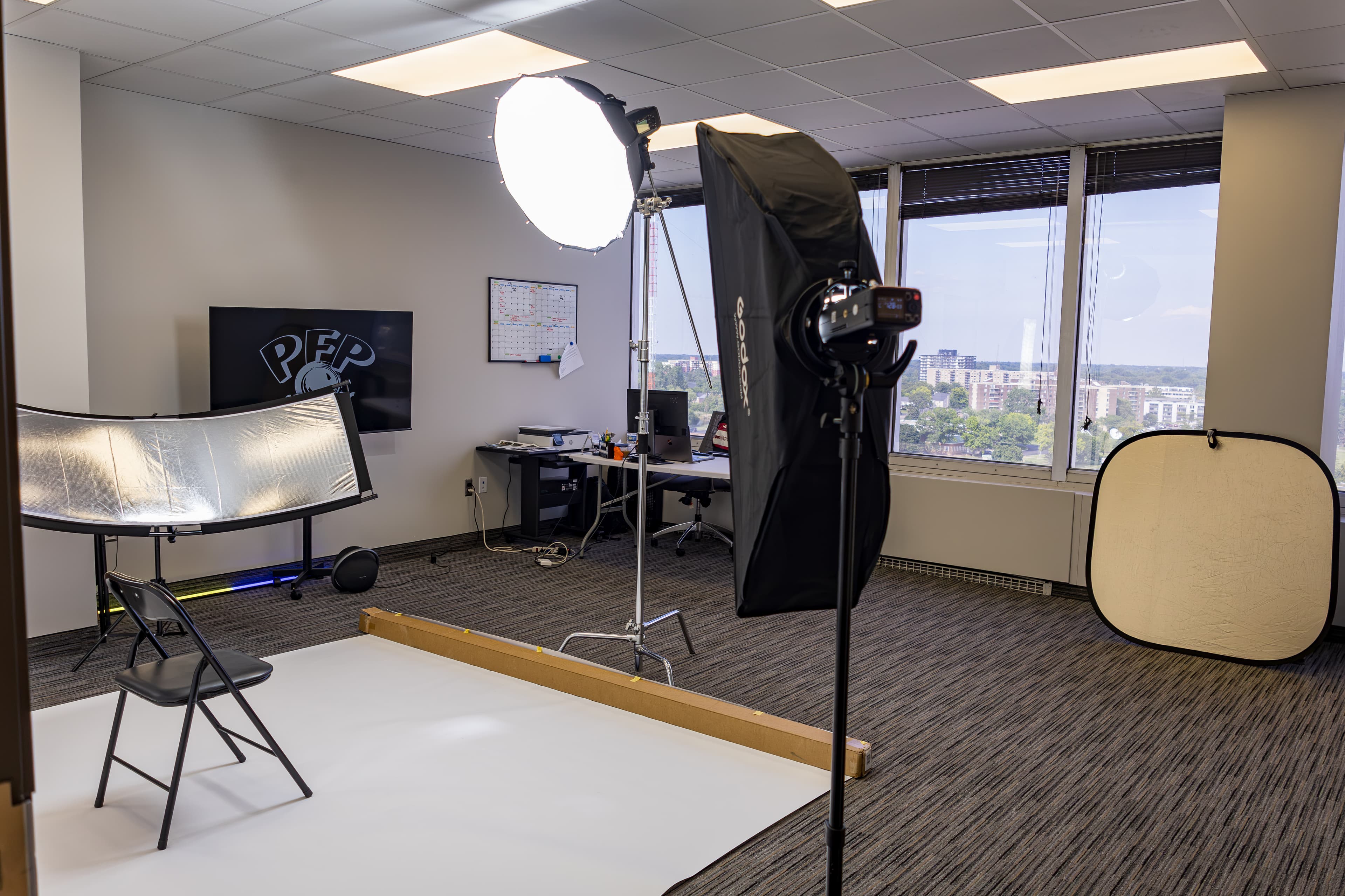 Professional photography studio setup in an office with lights, reflectors, and a white backdrop.