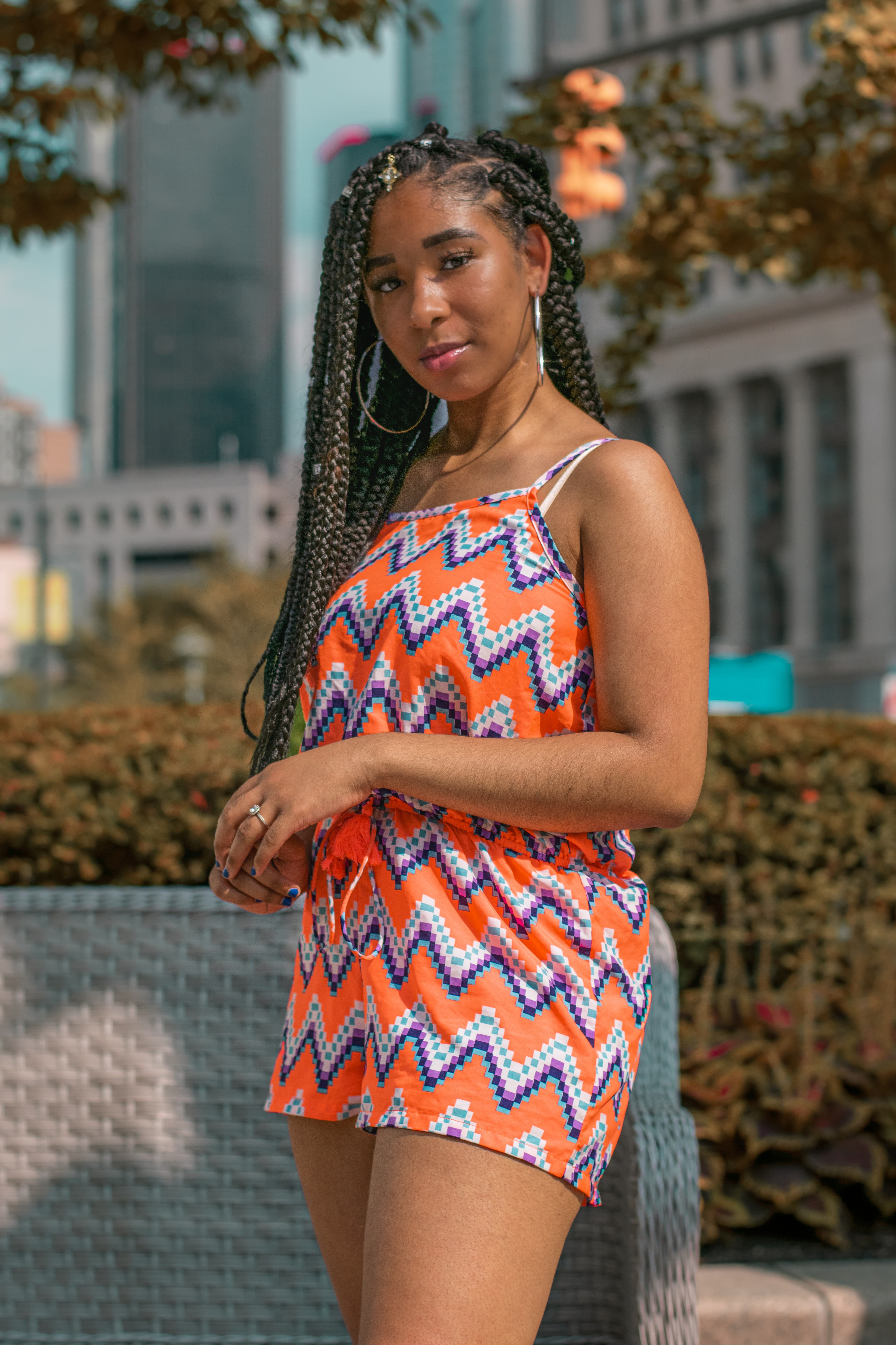 Young woman with long box braids wearing a vibrant orange zigzag romper in the city.