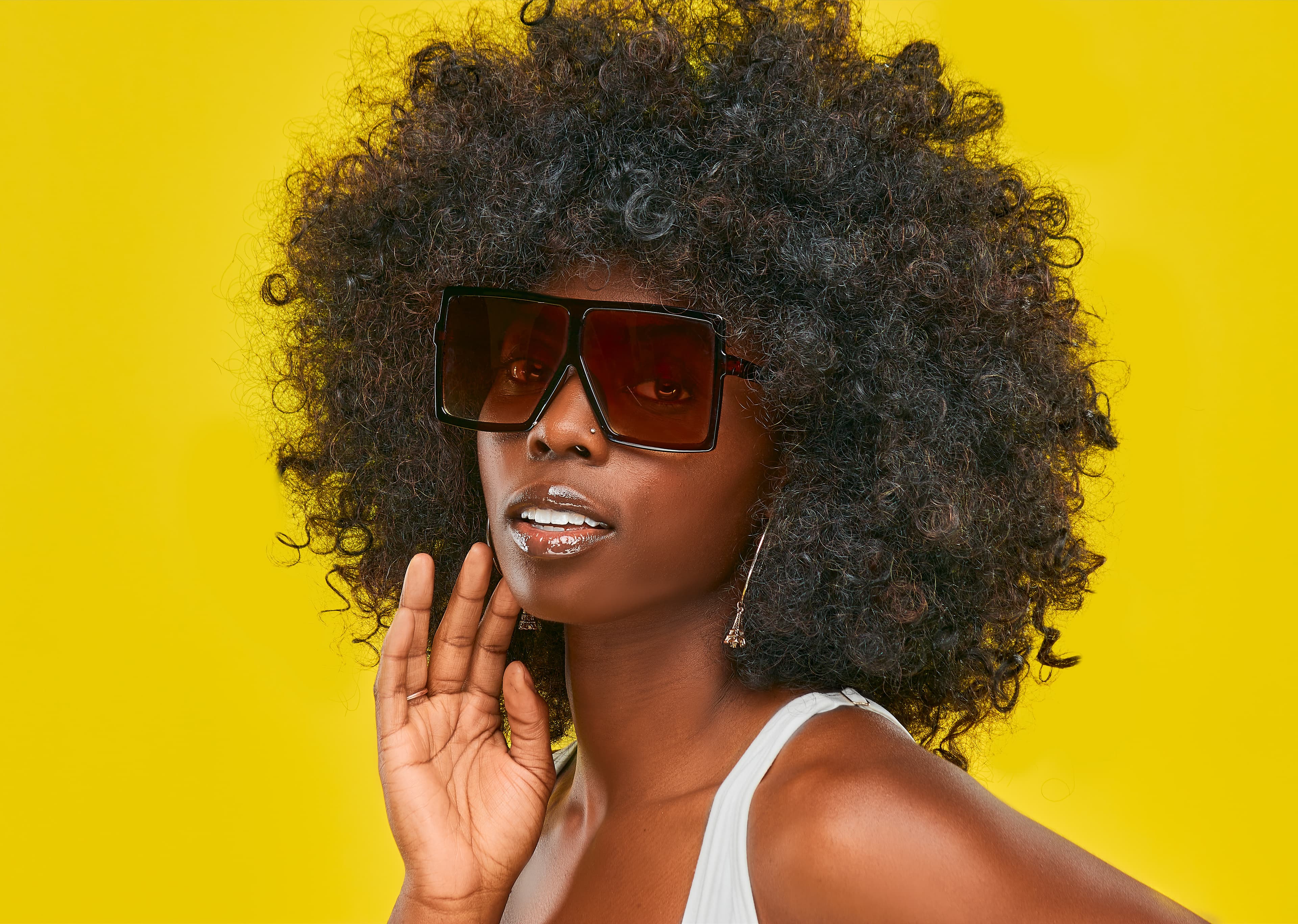 Black woman with a large afro and oversized sunglasses against a bright yellow background.
