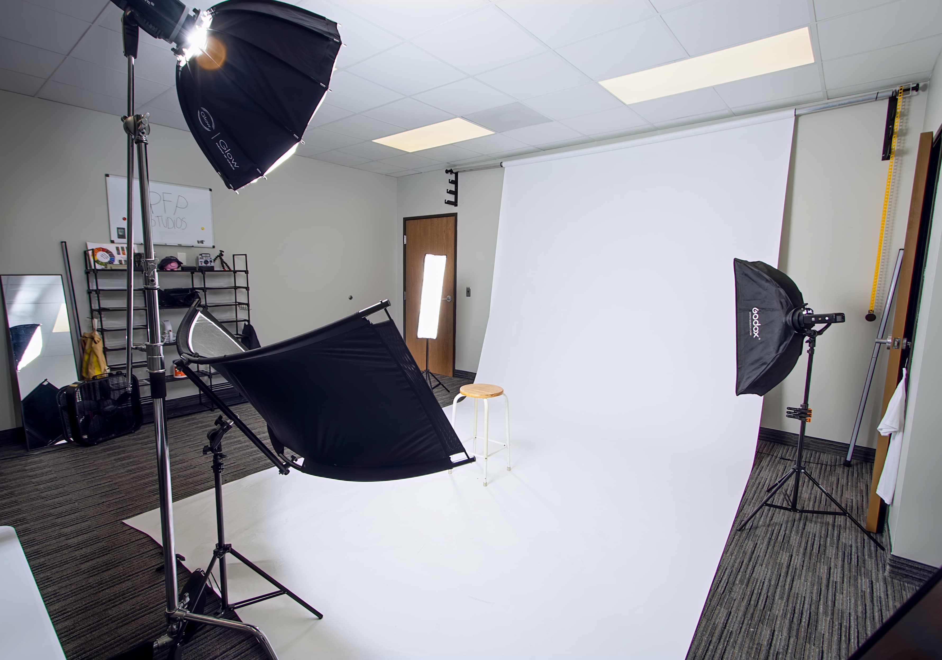 Professional photo studio with a white backdrop, studio lights, and a small wooden stool.
