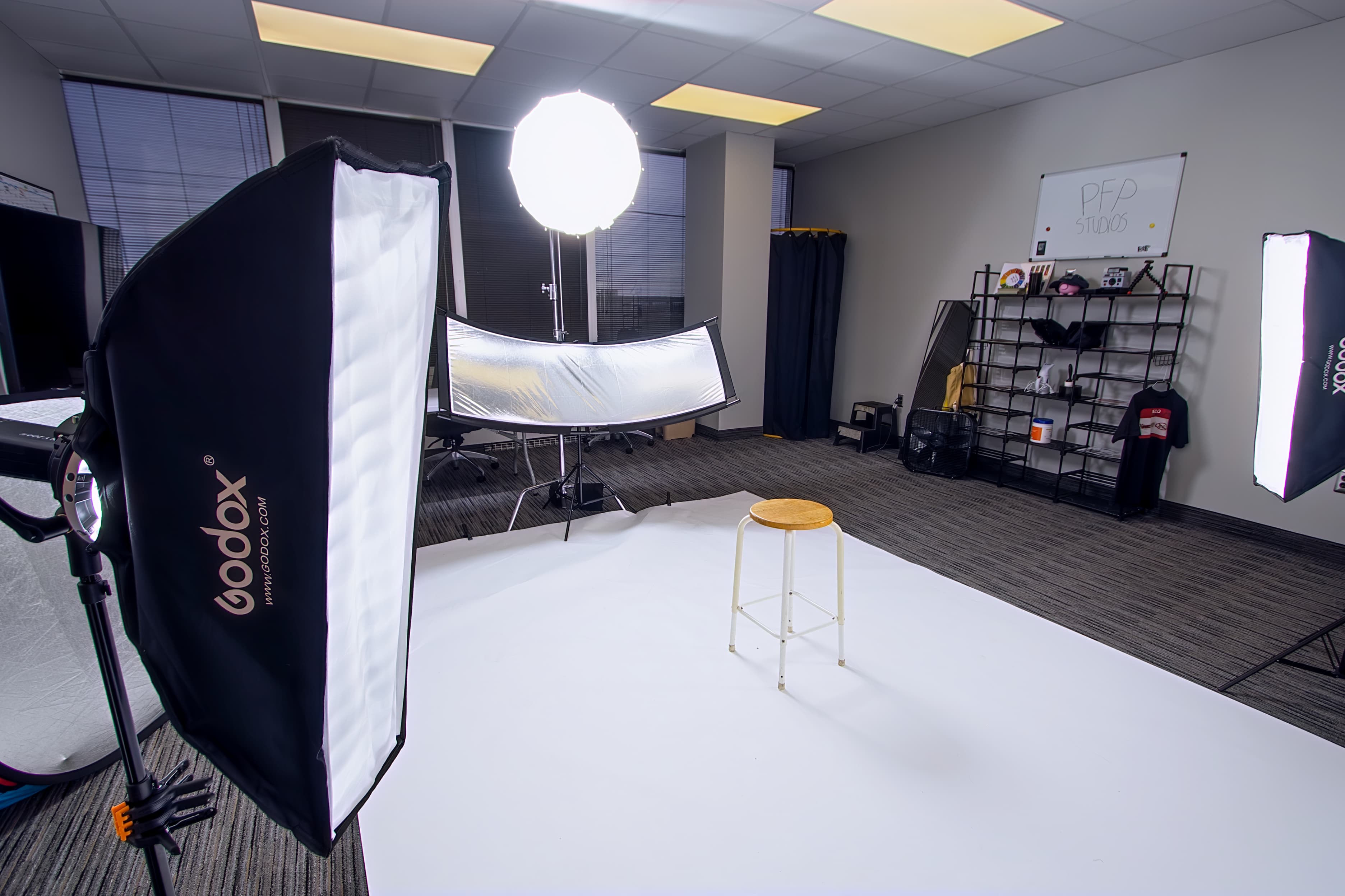 Professional photography studio setup featuring a white backdrop, wooden stool, and Godox lighting equipment.