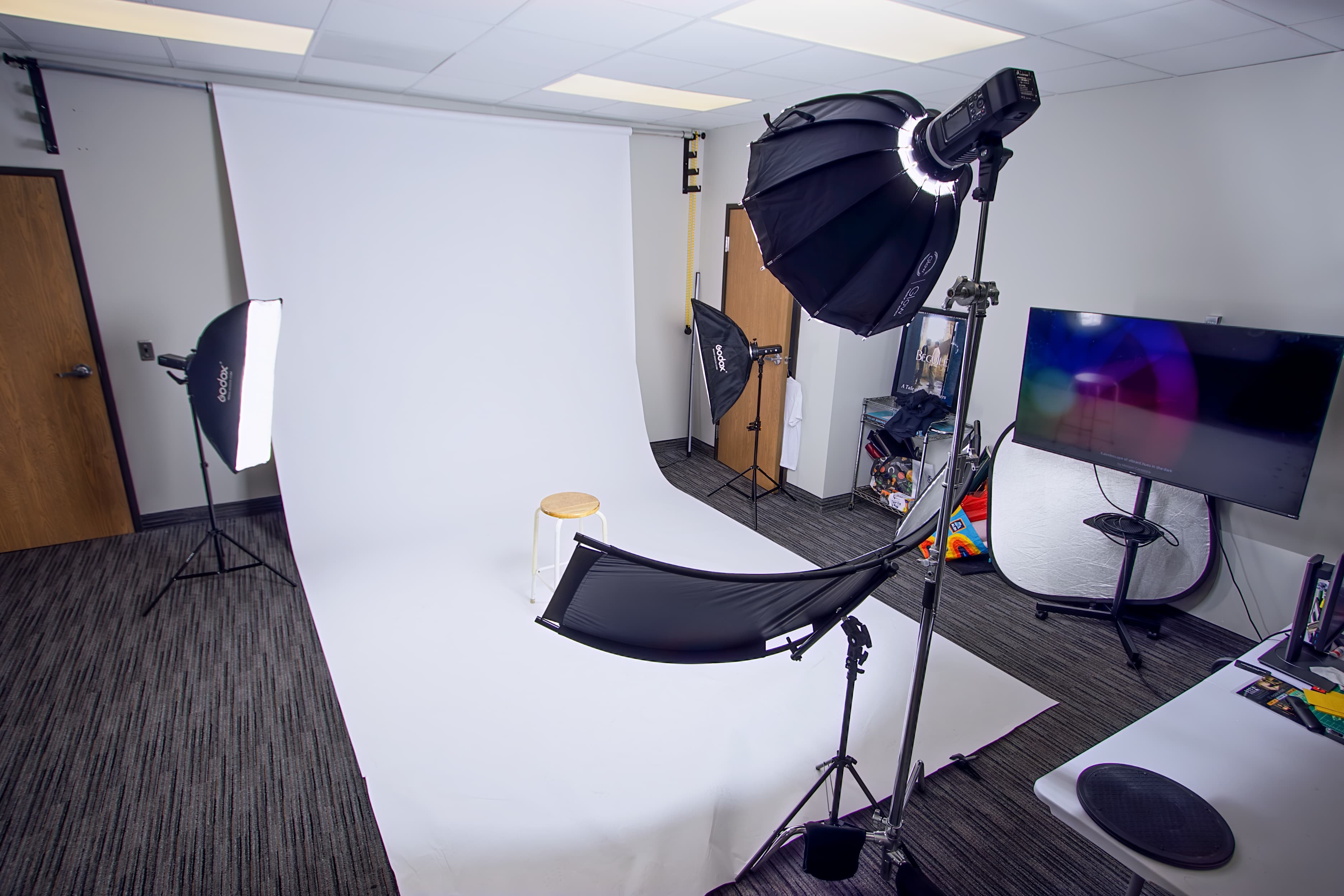 Professional photography studio with a white backdrop, wooden stool, and multiple studio softbox lights.