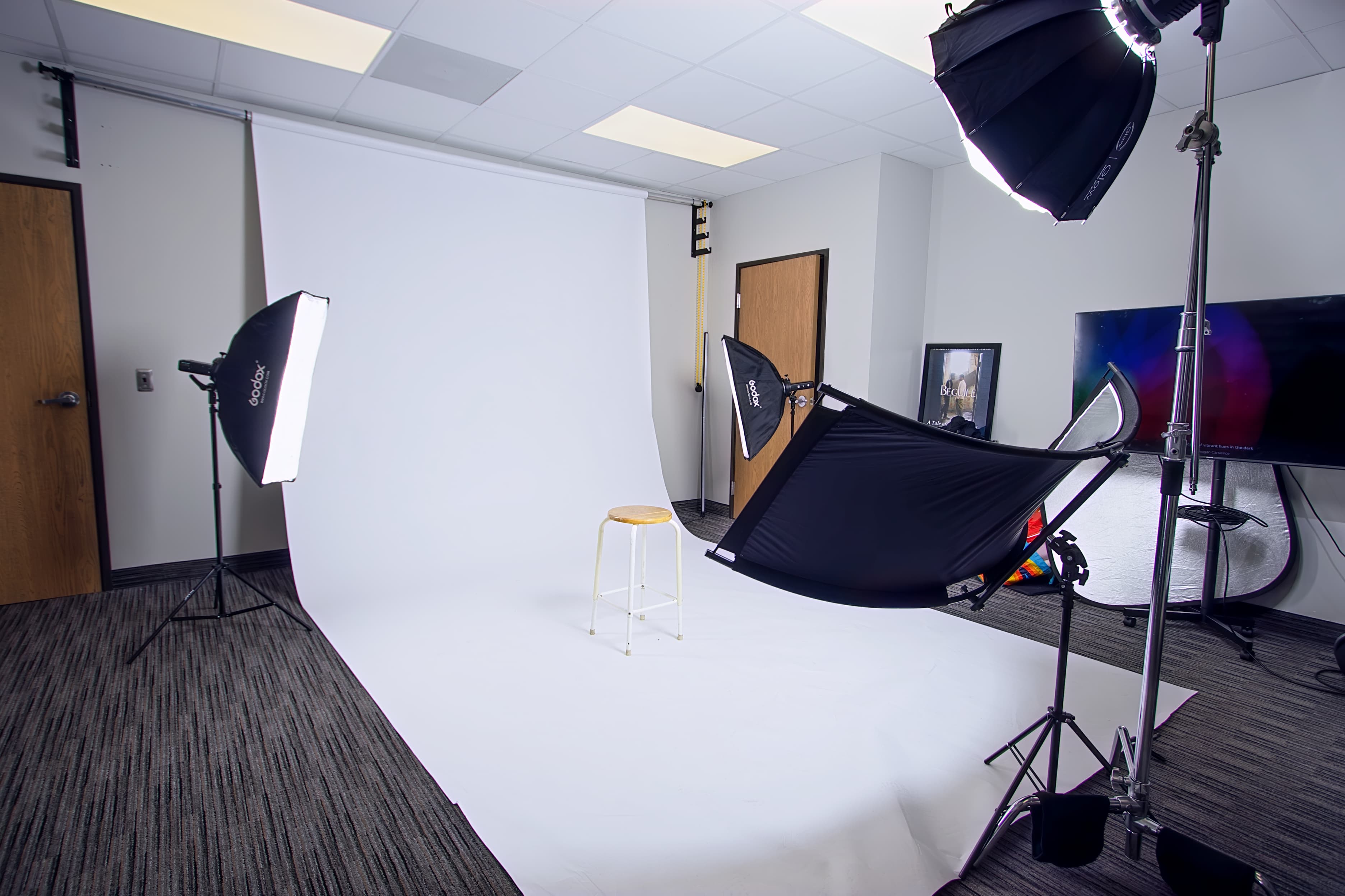 Professional photography studio featuring a white backdrop, wooden stool, and multiple softbox lights on stands.